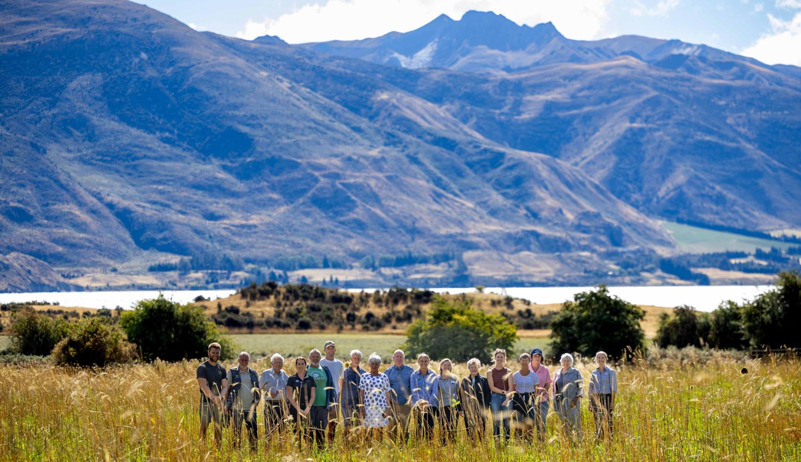 Group standing in a golden tussock meadow with mountains and a lake behind.