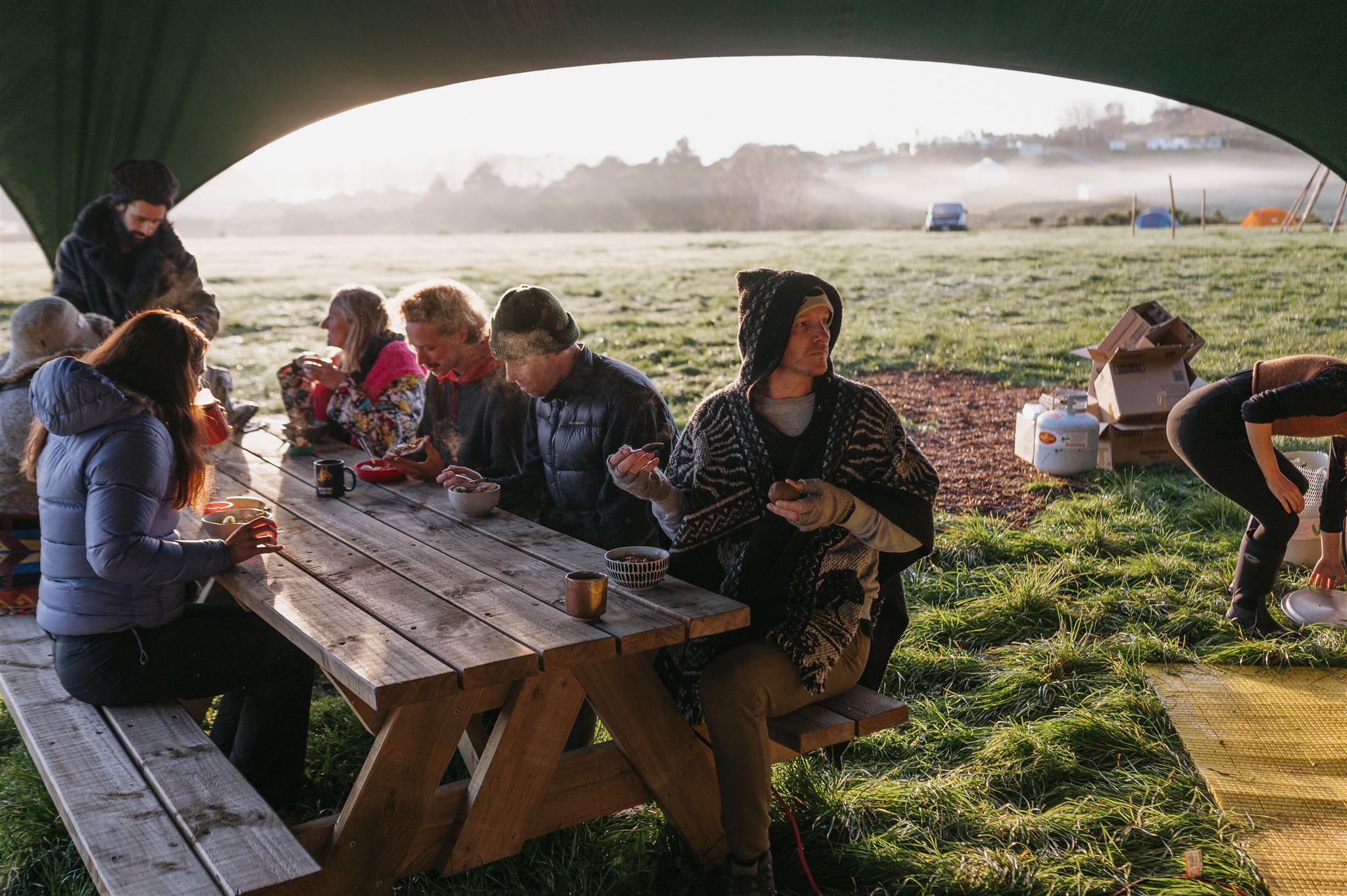 Shared breakfast at a picnic table under a marquee at dawn.